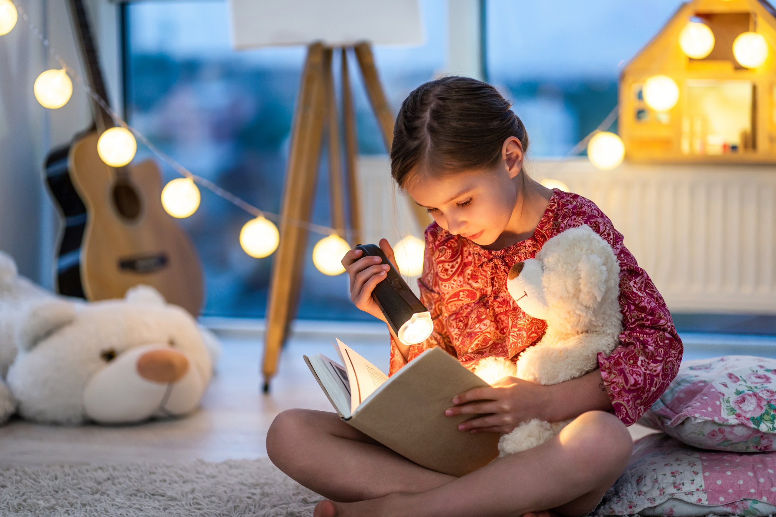Beautiful brown hair toddler girl reads a book with flashlight i